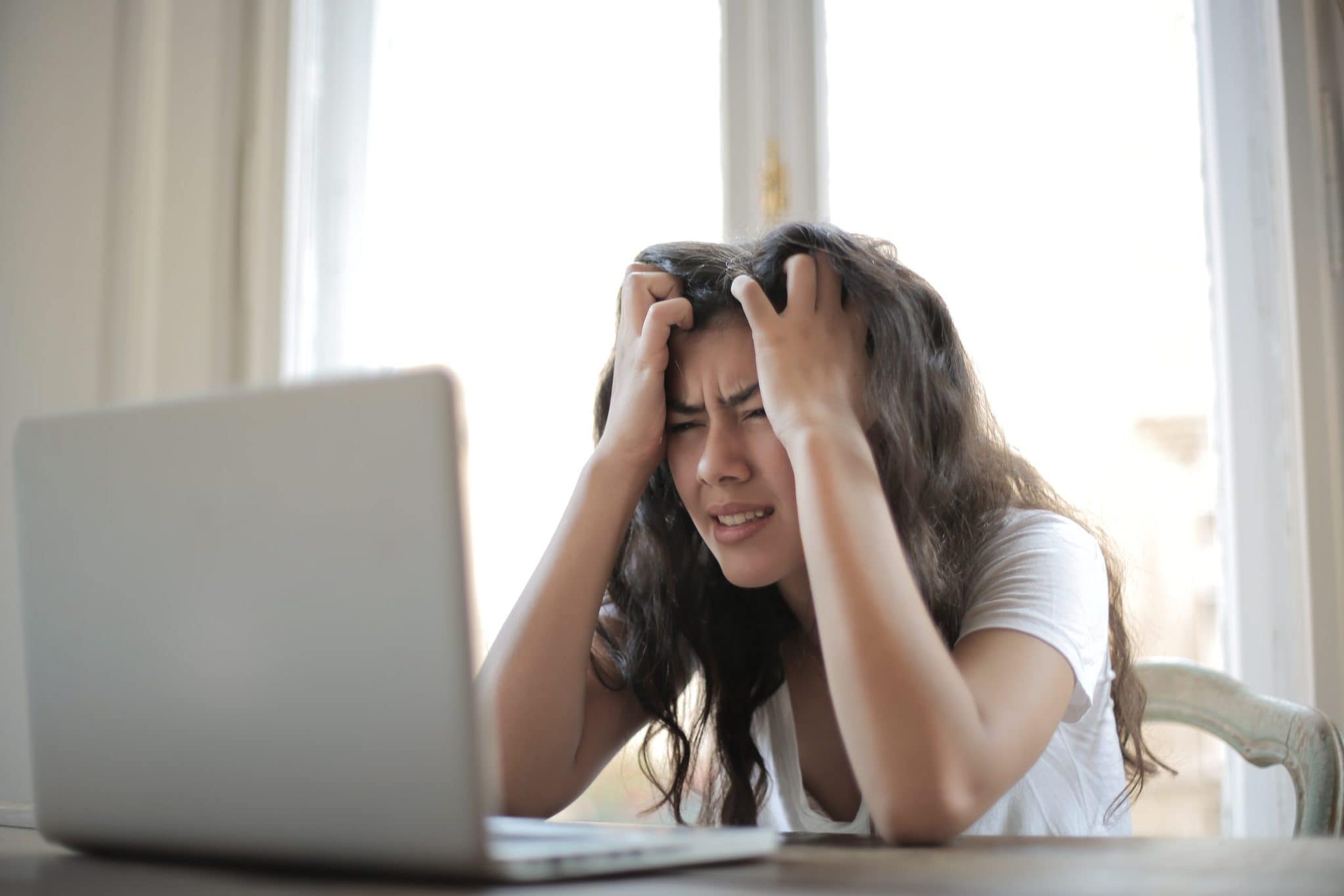 Woman with long brown hair grabbing her hair in frustration staring at a computer 