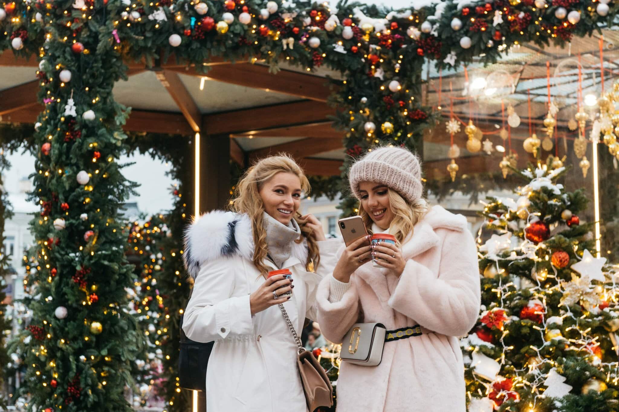 two women looking at their phones with a holiday background - holiday tips Venturewrite blog