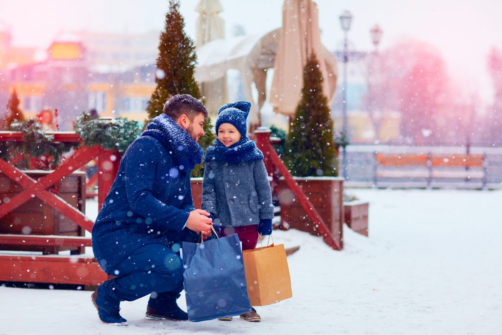 A dad and his son outside of a Christmas tree farm with shopping bags in the snow. Holiday shopping 