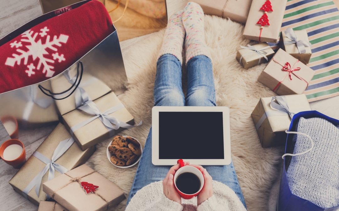 person surrounded by presents with a cup of coffee and a blank ipad on their lap holiday shopping
